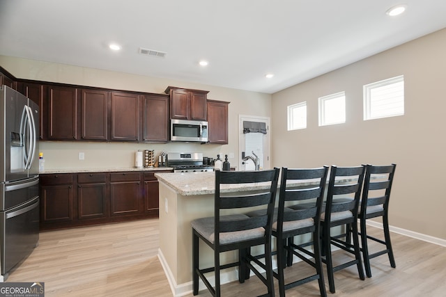 kitchen featuring light wood-style flooring, a kitchen bar, a center island with sink, and appliances with stainless steel finishes