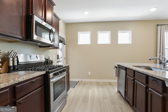 kitchen featuring baseboards, a sink, appliances with stainless steel finishes, light wood-style floors, and light stone counters