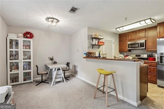 kitchen featuring brown cabinetry, a textured ceiling, visible vents, a breakfast bar, and appliances with stainless steel finishes