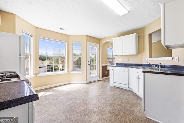 1016 Borrington Ln, Stockbridge, GA 30281 - kitchen featuring white appliances, a textured ceiling, plenty of natural light, white cabinetry, and arched walkways