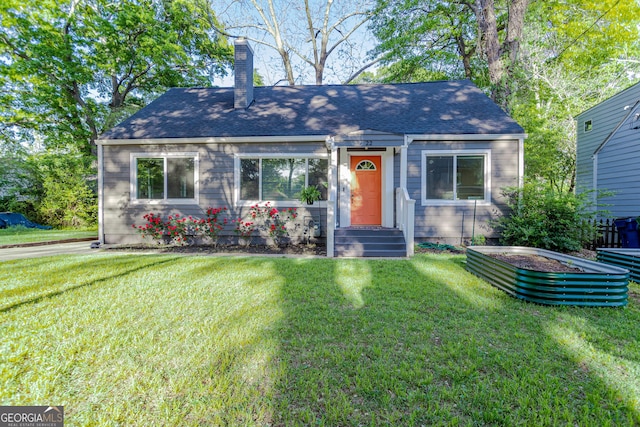 view of front of house with a shingled roof, a chimney, and a front yard