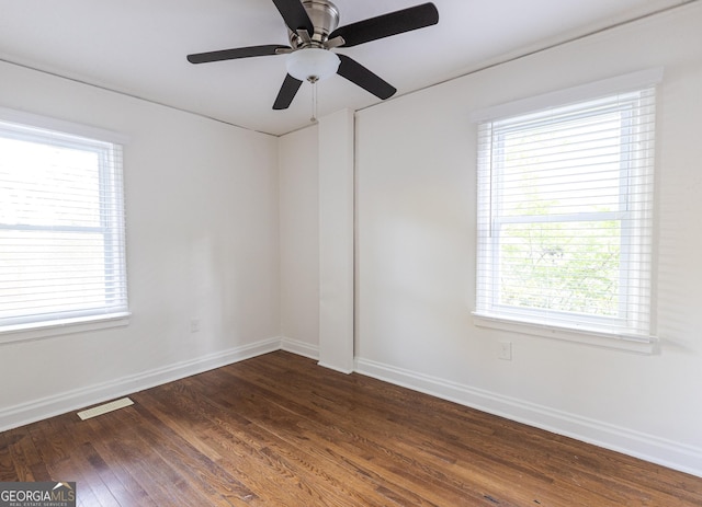 spare room featuring a wealth of natural light, dark wood-type flooring, visible vents, and baseboards