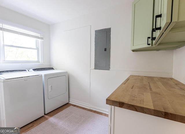 clothes washing area featuring separate washer and dryer, electric panel, wood finished floors, and cabinet space