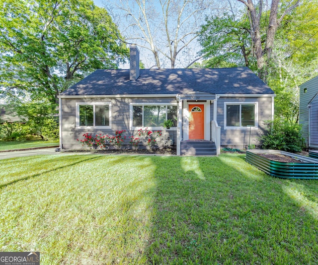view of front facade with a front yard, a shingled roof, and a chimney
