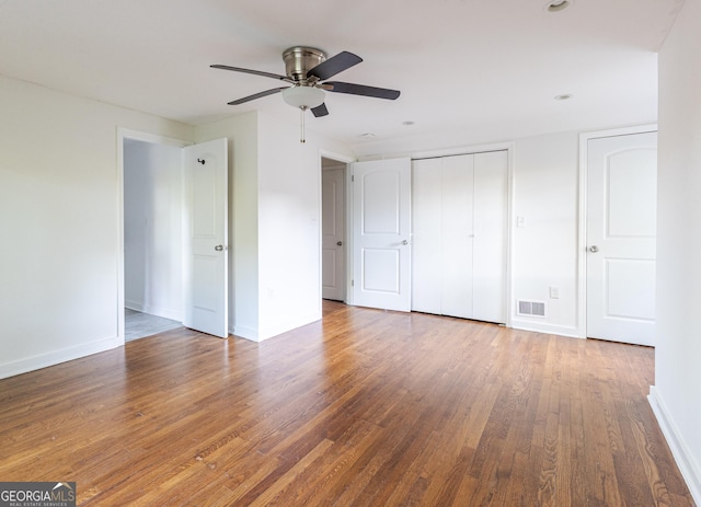 unfurnished bedroom featuring baseboards, wood finished floors, visible vents, and a closet