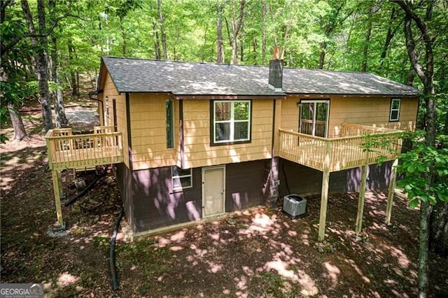 rear view of property with a shingled roof, a wooden deck, and a wooded view