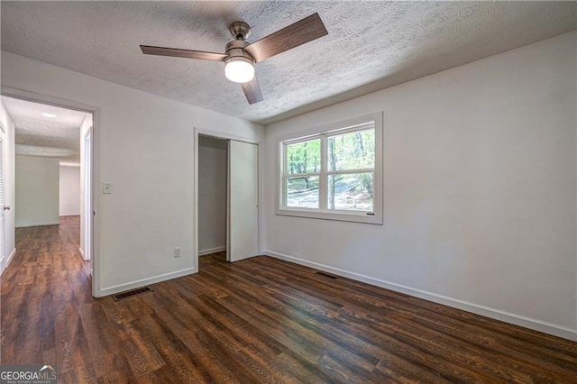 unfurnished bedroom featuring a closet, baseboards, dark wood-style floors, a textured ceiling, and visible vents