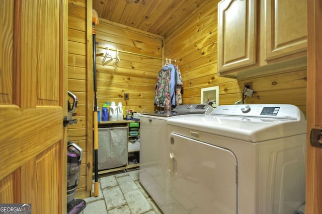 laundry area featuring stone finish floor, wood ceiling, independent washer and dryer, cabinet space, and wood walls