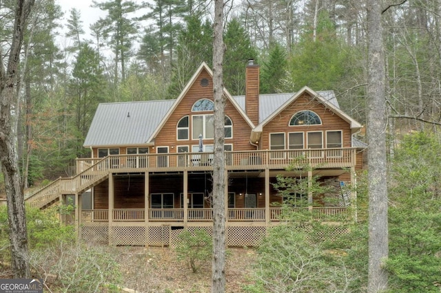 back of property featuring a wooden deck, stairway, metal roof, log veneer siding, and a chimney