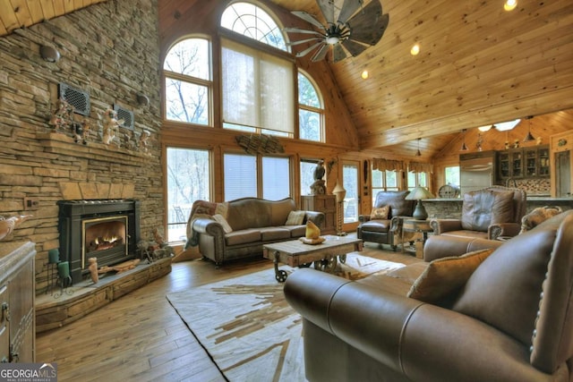 living area featuring wood-type flooring, a ceiling fan, a stone fireplace, and a wealth of natural light