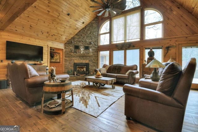 living area with wooden walls, a healthy amount of sunlight, wood-type flooring, wooden ceiling, and ceiling fan