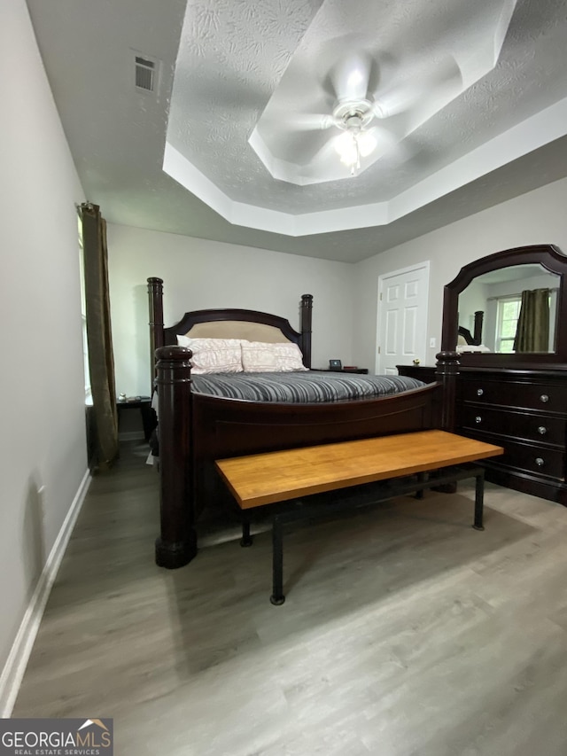bedroom featuring a tray ceiling, wood finished floors, visible vents, and a textured ceiling