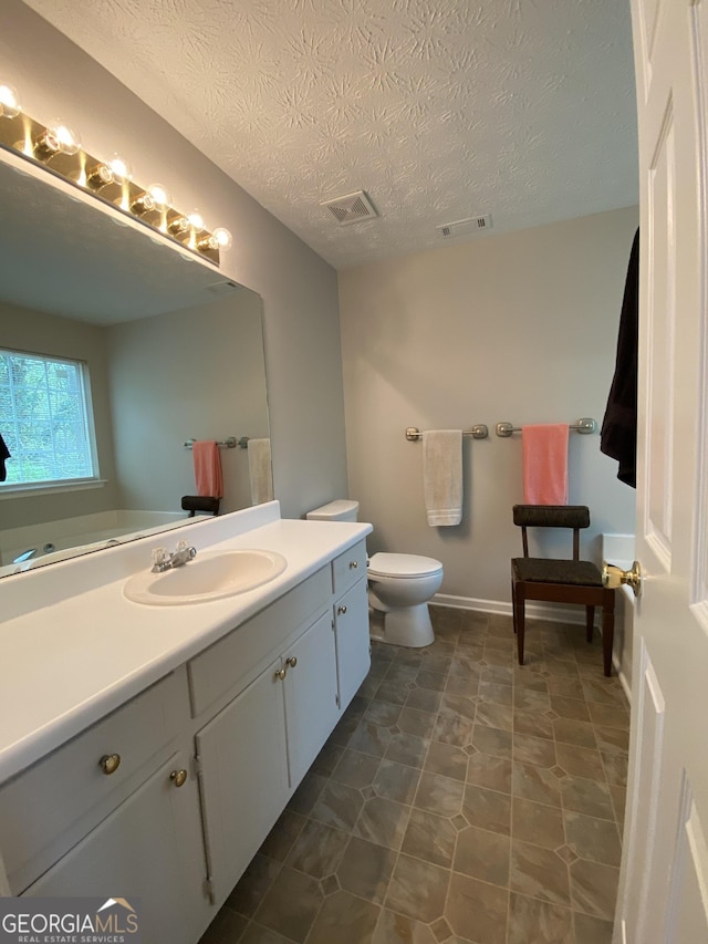 bathroom featuring visible vents, toilet, vanity, and a textured ceiling