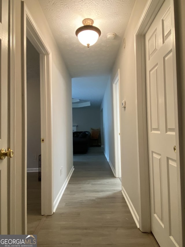 corridor with a textured ceiling, baseboards, and wood finished floors