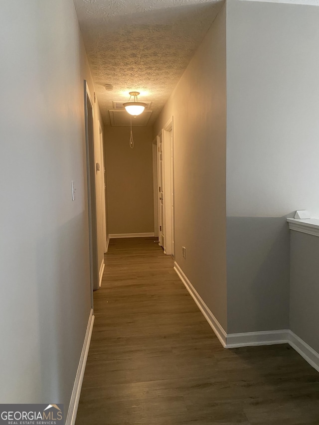hallway with baseboards, wood finished floors, and a textured ceiling