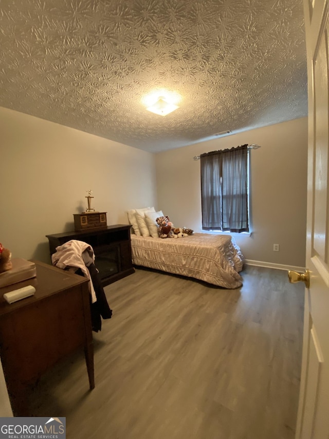 bedroom featuring a textured ceiling, wood finished floors, baseboards, and visible vents