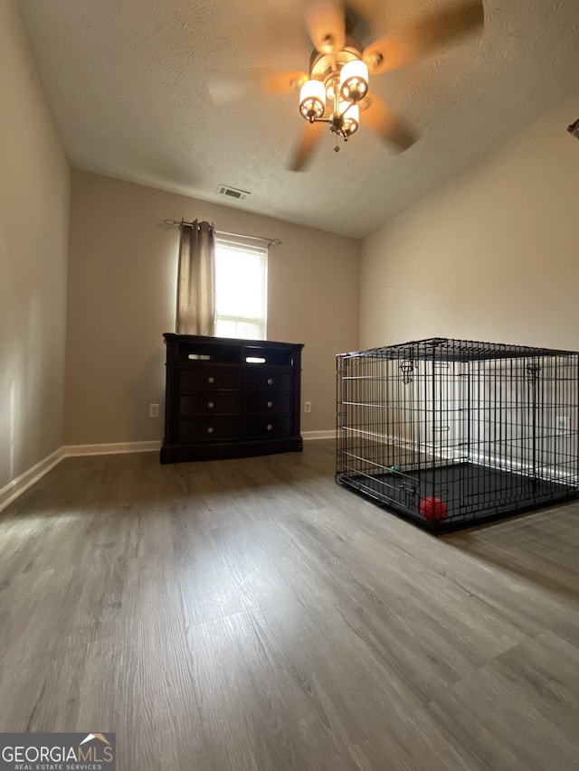 unfurnished bedroom with a textured ceiling, wood finished floors, baseboards, and visible vents