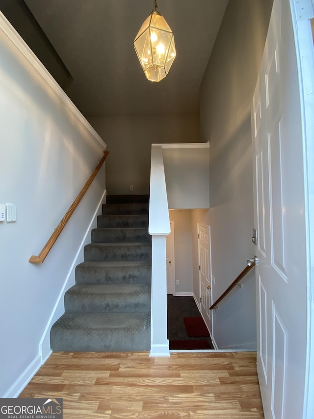 staircase with wood finished floors, a notable chandelier, and baseboards