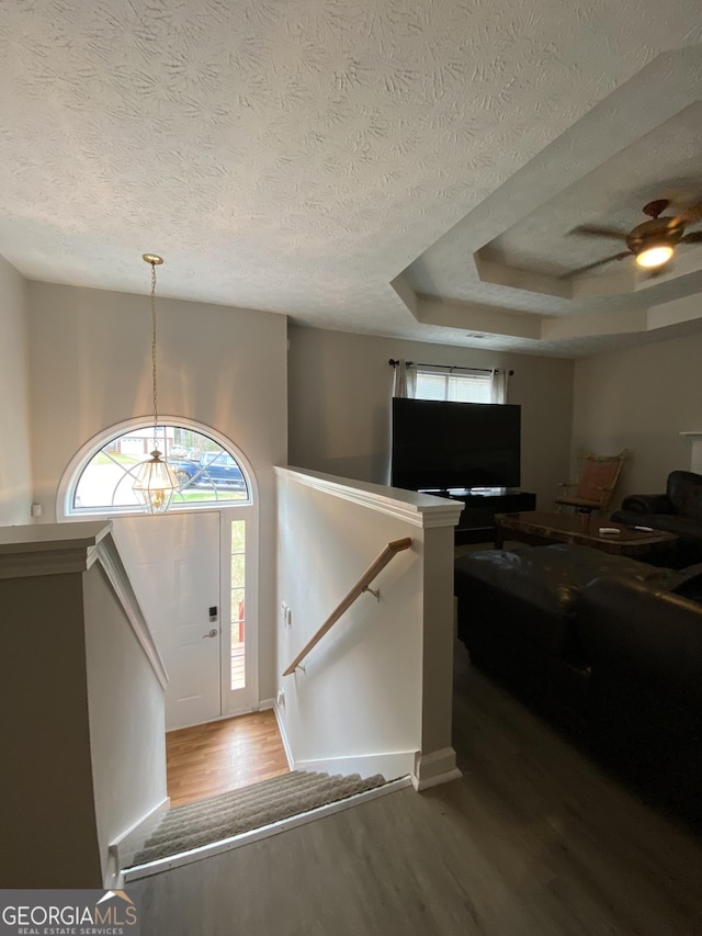 entryway with ceiling fan, a tray ceiling, a textured ceiling, and wood finished floors