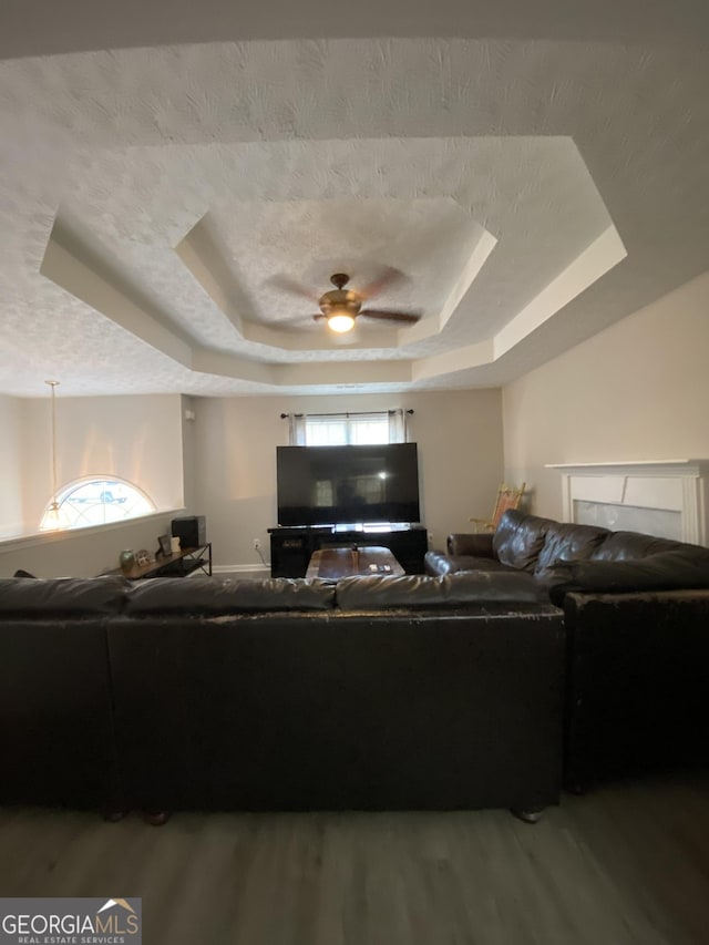 living room featuring a tray ceiling, a textured ceiling, a ceiling fan, and wood finished floors