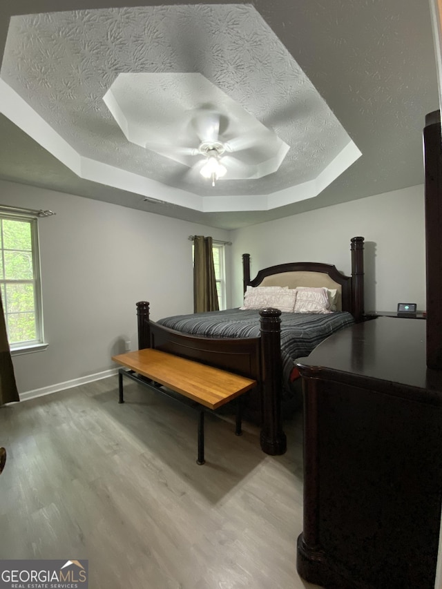 bedroom featuring light wood-type flooring, a textured ceiling, and a raised ceiling