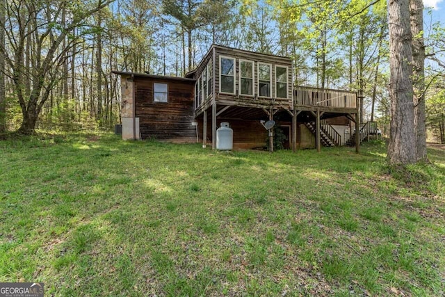 rear view of property with a sunroom, a lawn, a wooden deck, and stairs