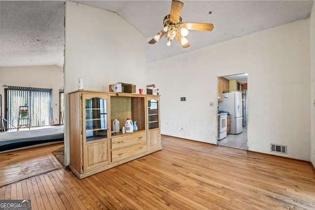 interior space with lofted ceiling, a textured ceiling, light wood-style floors, visible vents, and ceiling fan