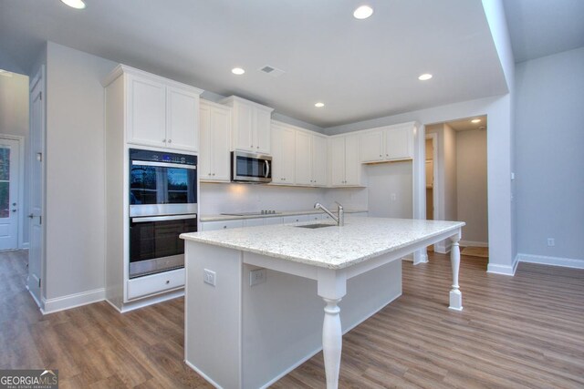 kitchen featuring white cabinets, recessed lighting, wood finished floors, a sink, and stainless steel appliances