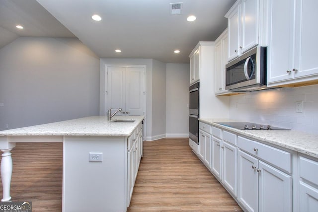 kitchen with stainless steel microwave, light wood-type flooring, white cabinetry, visible vents, and a sink