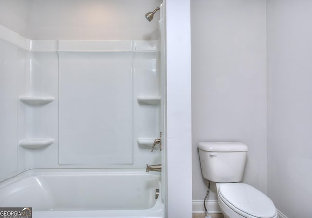 bathroom featuring toilet, baseboards, and  shower combination