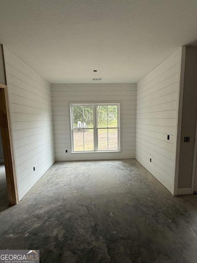 empty room featuring concrete floors, wood walls, and a textured ceiling