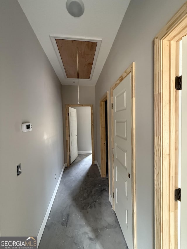 hall with attic access, concrete floors, and baseboards