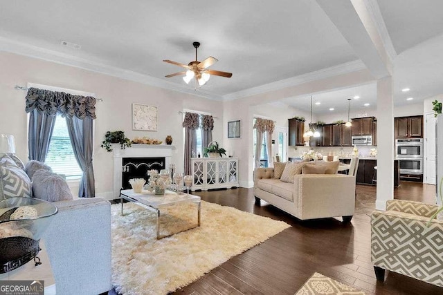 living room featuring baseboards, a fireplace, a ceiling fan, crown molding, and dark wood-type flooring