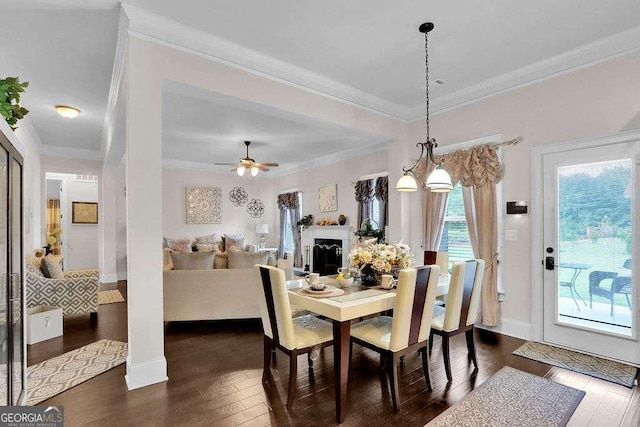 dining room with baseboards, ornamental molding, a ceiling fan, a fireplace, and dark wood-style floors