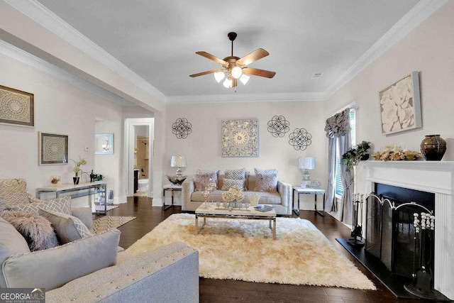living room featuring ceiling fan, dark wood-type flooring, ornamental molding, a fireplace with raised hearth, and baseboards