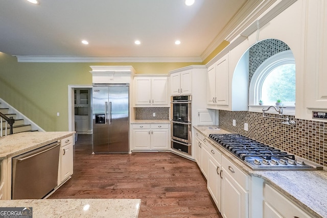 kitchen featuring white cabinets, appliances with stainless steel finishes, tasteful backsplash, and ornamental molding
