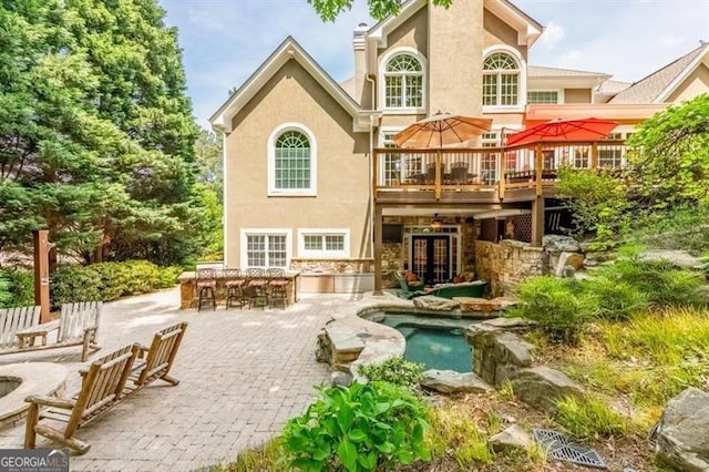 rear view of property featuring outdoor dry bar, a patio, stucco siding, and a wooden deck