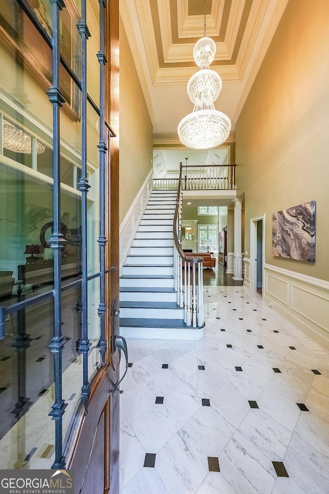 foyer entrance featuring a tray ceiling, a notable chandelier, crown molding, a decorative wall, and stairs