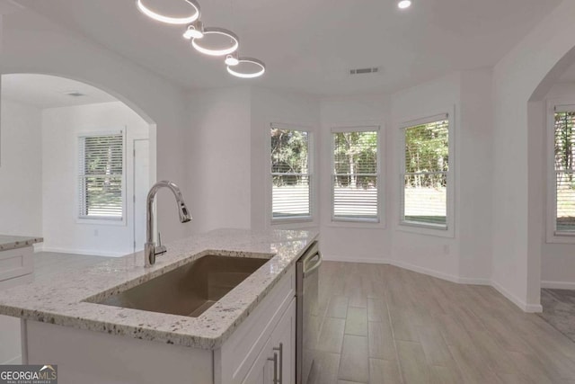 4066 Wild Orchid Ln, Loganville, GA 30052 - kitchen featuring white cabinetry, light stone countertops, arched walkways, dishwasher, and a sink