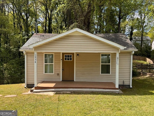 view of front of house featuring fence, a shingled roof, a front lawn, and covered porch