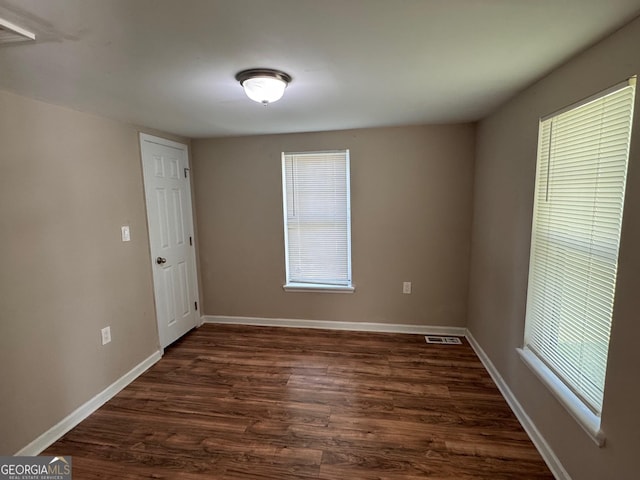 unfurnished room featuring dark wood-type flooring, visible vents, and baseboards
