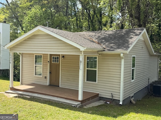 view of front of house with central air condition unit, a porch, a shingled roof, and a front yard