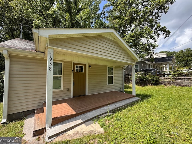 view of front facade featuring covered porch, a shingled roof, a front lawn, and fence