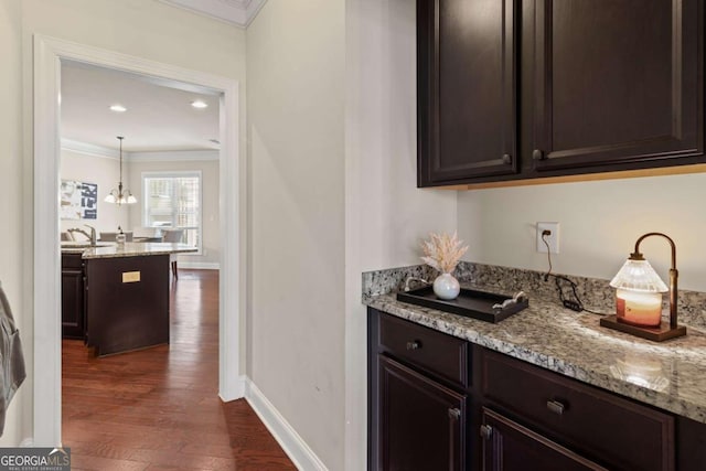 bar with baseboards, an inviting chandelier, dark wood-style floors, crown molding, and pendant lighting