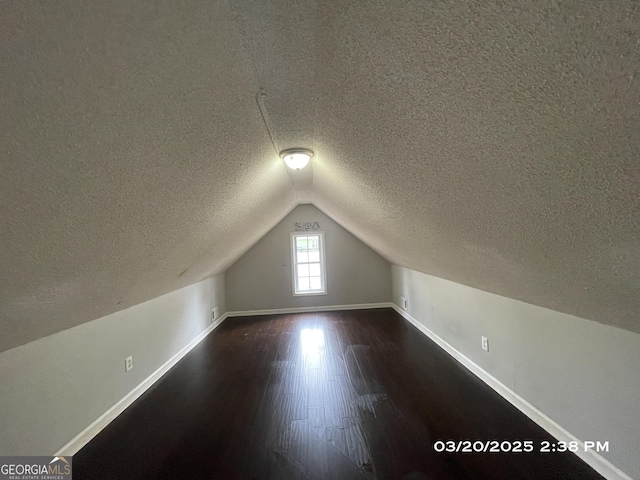 135 Flowers Dr, Covington, GA 30016 - additional living space with a textured ceiling, dark wood-style flooring, baseboards, and vaulted ceiling