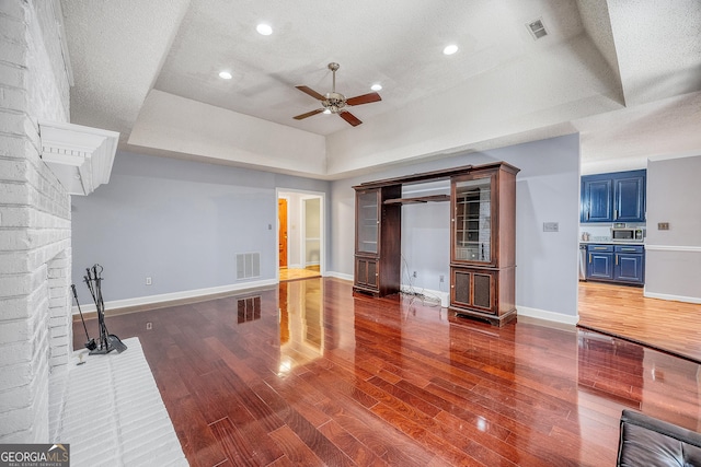 unfurnished living room with a raised ceiling, ceiling fan, wood finished floors, and visible vents