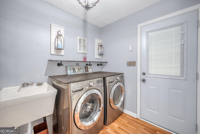 laundry area with laundry area, a textured ceiling, washing machine and dryer, a sink, and light wood finished floors