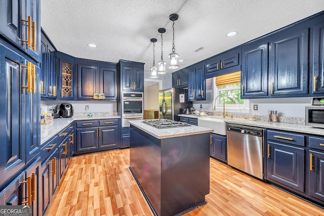 kitchen featuring a textured ceiling, appliances with stainless steel finishes, a sink, a warming drawer, and light wood-style flooring