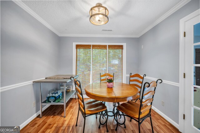 dining area with a textured ceiling, baseboards, wood finished floors, visible vents, and ornamental molding