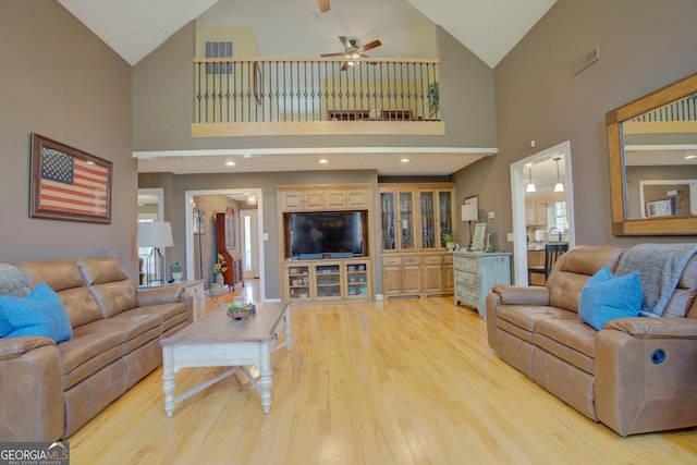 living room featuring vaulted ceiling, light wood-style floors, visible vents, and a ceiling fan